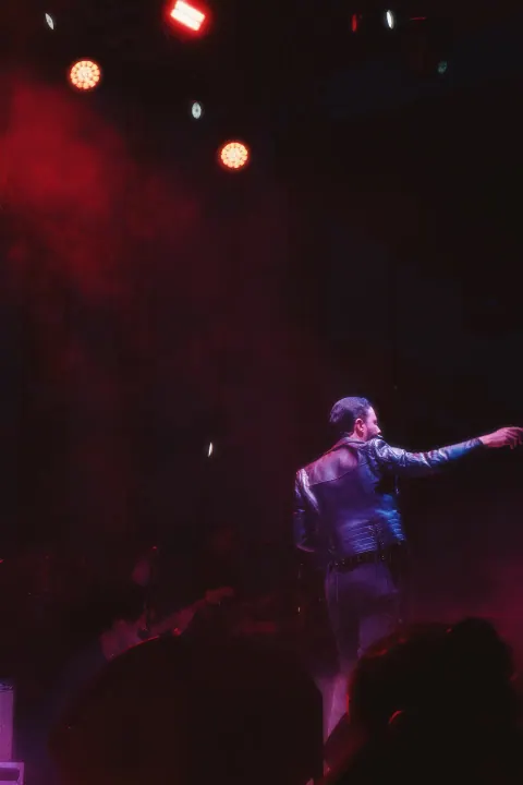 Cantante saludando al público bajo la iluminación roja del escenario.