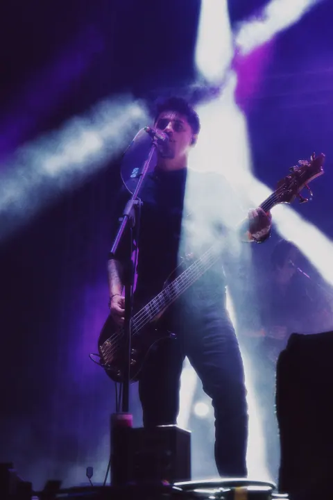 Guitarrista frente al micrófono bajo luces violetas y blancas.